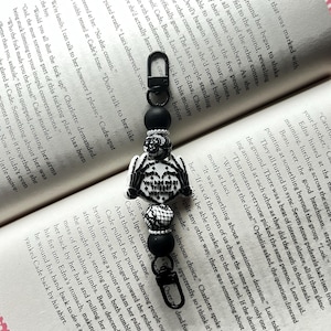 May include: Black and white keychain with a skeleton hand charm, a black heart with a skull and crossbones, and the text "You had me at Warn" on a black and white beaded chain.