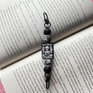 May include: Black and white beaded keychain with a black and white skull charm. The charm has the text "I Use Trigger Warnings As A Checklist".