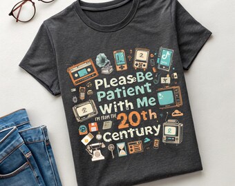 以下が含まれることがあります： ヴィンテージエレクトロニクスと「Please Be Patient With Me, I'm From The 20th Century」のテキストが特徴の、カラフルなグラフィックデザインの濃い灰色のTシャツ。デザインには、カセットテープ、テレビ、電話が含まれています。