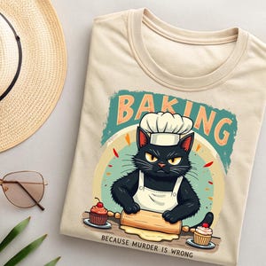 May include: A beige t-shirt with a black cat wearing a chef's hat and apron, rolling out dough with a rolling pin. The text "Baking because murder is wrong" is printed below the cat.