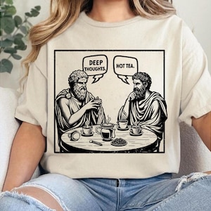 Könnte beinhalten: Beiges T-Shirt mit einer schwarz-weißen Grafik von zwei klassischen Figuren an einem Tisch mit Kaffeetassen. Sprechblasen darüber zeigen "Deep Thoughts" und "Hot Tea."