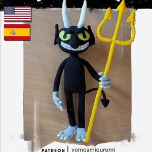 Puede incluir: Un juguete de amigurumi de crochet negro del Diablo del videojuego Cuphead. El Diablo sostiene un tridente de crochet amarillo. El juguete está de pie sobre una superficie de madera. La imagen también incluye el texto "The Devil" y el texto "yomoamigurumi".