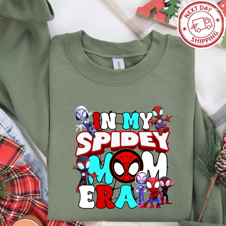 Puede incluir: Sudadera verde con un gr&aacute;fico de personajes de Spider-Man y el texto "In My Spidey Mom Era".