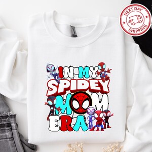 Puede incluir: Camiseta blanca de manga larga con un gr&aacute;fico colorido de personajes de Spider-Man y el texto "In My Spidey Mom Era".