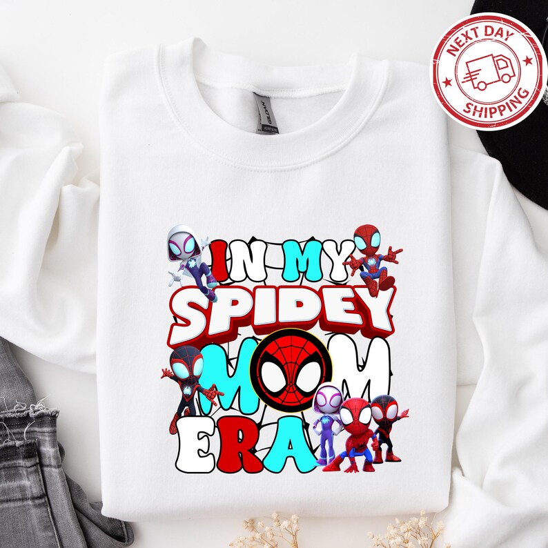 Puede incluir: Camiseta blanca de manga larga con un gr&aacute;fico colorido de personajes de Spider-Man y el texto "In My Spidey Mom Era".