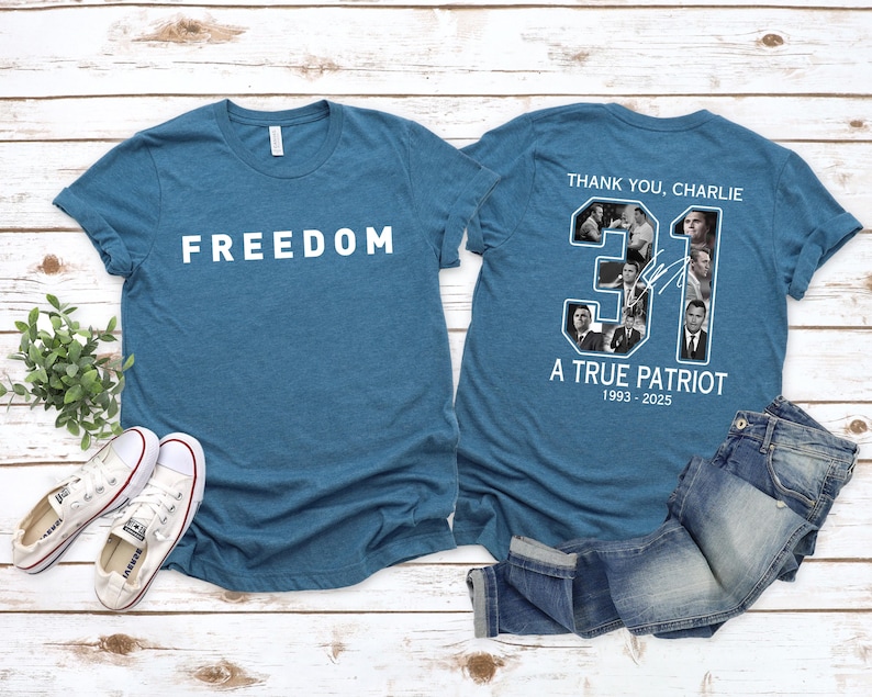 K&ouml;nnte beinhalten: T&uuml;rkisfarbene T-Shirts mit wei&szlig;em Text, der "FREEDOM" und "THANK YOU, CHARLIE" lautet. Auf der R&uuml;ckseite des Shirts befindet sich eine Collage von Bildern und der Text "31 A TRUE PATRIOT 1993-2025". Ein Paar wei&szlig;e Turnschuhe und blaue Jeans sind ebenfalls im Bild.