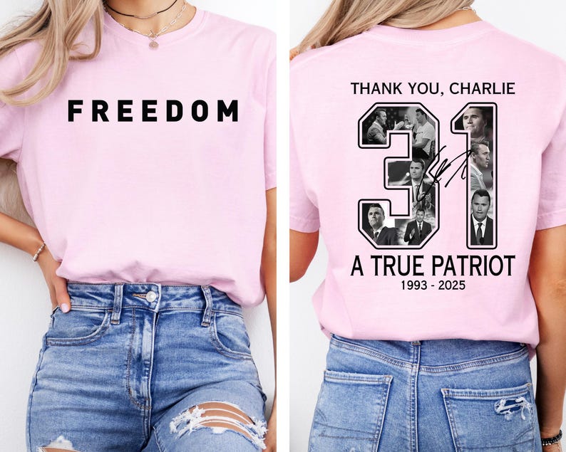 K&ouml;nnte beinhalten: Ein hellrosa T-Shirt mit dem Wort "FREEDOM" in fetten schwarzen Buchstaben auf der Vorderseite. Auf der R&uuml;ckseite des T-Shirts steht der Text "THANK YOU, CHARLIE" &uuml;ber der Zahl "31" mit Bildern und dem Text "A TRUE PATRIOT 1993-2025".