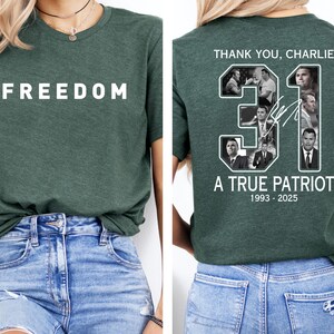 K&ouml;nnte beinhalten: Ein dunkelgr&uuml;nes T-Shirt mit dem Wort "FREEDOM" in wei&szlig;en Blockbuchstaben auf der Vorderseite. Die R&uuml;ckseite des Shirts zeigt ein Design mit dem Text "THANK YOU, CHARLIE", der Zahl "31" mit Bildern und dem Text "A TRUE PATRIOT 1993-2025".