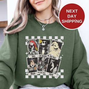 May include: Green sweatshirt with a checkered background and a graphic of characters from the Nightmare Before Christmas. The characters are depicted as playing cards with their names below each card: Sally, Jack Skellington, Oogie Boogie, Mayor, Lock Shock Barrel, and Zero.