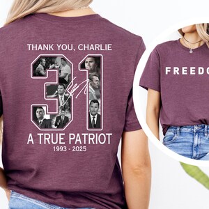 K&ouml;nnte beinhalten: Burgunderfarbenes T-Shirt mit dem wei&szlig;en Schriftzug "FREEDOM" auf der Vorderseite. Auf der R&uuml;ckseite des Shirts stehen die Worte "THANK YOU, CHARLIE", die Zahl "31" und der Text "A TRUE PATRIOT 1993-2025".