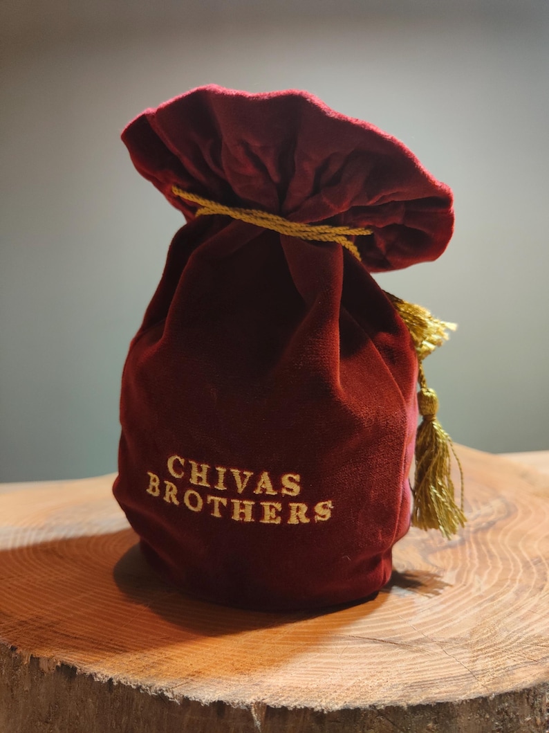 May include: A red velvet bag with a gold drawstring and tassel. The bag has the words "CHIVAS BROTHERS" embroidered on the front in gold thread.