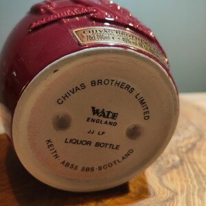 May include: A red ceramic liquor bottle with a white label that reads "CHIVAS BROTHERS LIMITED" and "WADE ENGLAND". The bottle is embossed with a design of a stag.