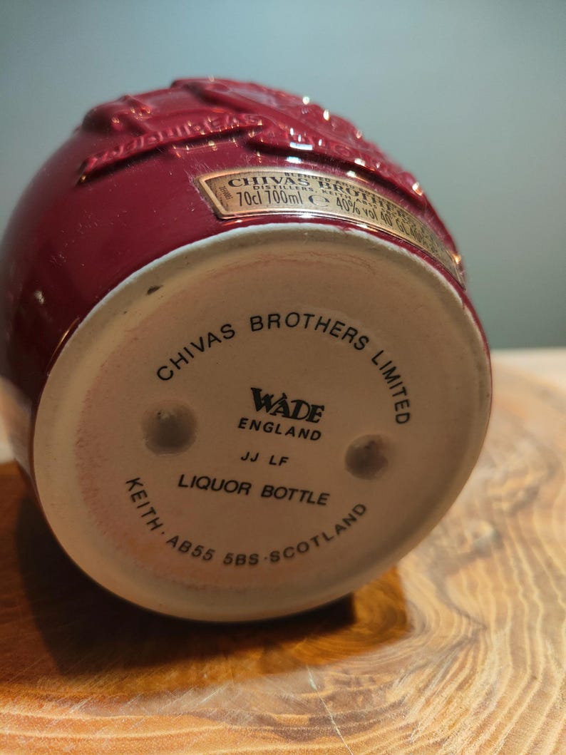 May include: A red ceramic liquor bottle with a white label that reads "CHIVAS BROTHERS LIMITED" and "WADE ENGLAND". The bottle is embossed with a design of a stag.