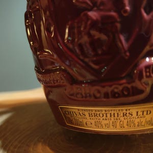 May include: A dark red bottle with a gold label that reads "BLENDED AND BOTTLED BY CHIVAS BROTHERS LTD DISTILLERS, KEITH ABSS SNS. SCOTLAND d 700ml e 40% vol 40&deg;GL 40% alc./vol."