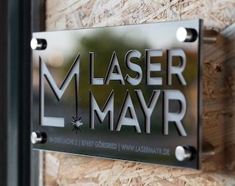 Könnte beinhalten: Ein schwarzes Schild mit dem Text "M LASER MAYR" in weißen Buchstaben. Das Schild ist an einer Holzwand befestigt.