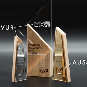 Op de afbeelding: Een houten award met een transparante acrylplaat. De plaat heeft de tekst "LASER MAYR" en een klein "M" logo. De houten basis heeft de tekst "MITARBEITER DES MONATS AUGUST 2025".