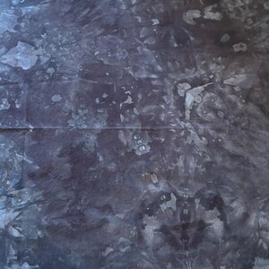 May include: A dark blue fabric with a tie-dye pattern. The fabric has a mottled appearance with lighter blue and white splotches throughout. The overall effect is a textured, abstract design.