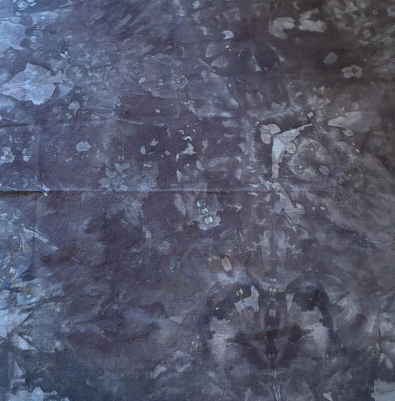 May include: A dark blue fabric with a tie-dye pattern. The fabric has a mottled appearance with lighter blue and white splotches throughout. The overall effect is a textured, abstract design.