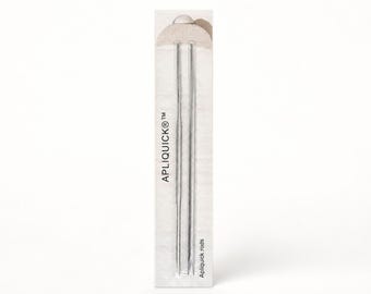 May include: Two thin, silver-colored metal rods for sewing and applique, packaged in a vertical rectangular cardboard sleeve. The packaging features the text APLIQUICK and Apliquick rods printed in black on a light, textured off-white background.