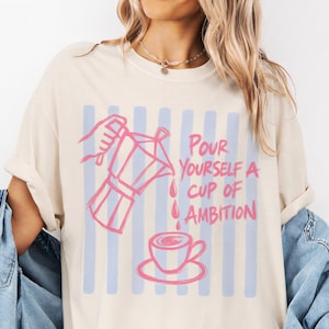 A woman wearing a white t-shirt with a graphic design and text printed on it.