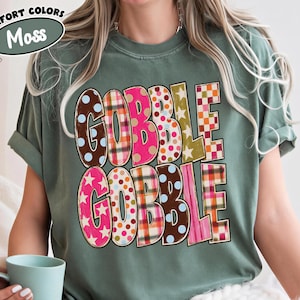 A person wearing a green t-shirt with the word "GOBBLE GOBBLE" printed on it, sitting on a bed with a cup of coffee.