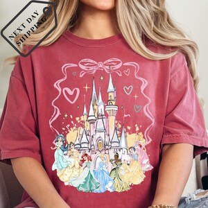 A person wearing a red t-shirt with a Disney princess castle design printed on it.