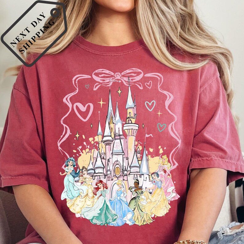 A person wearing a red t-shirt with a Disney princess castle design printed on it.