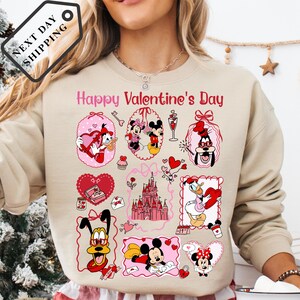 A woman wearing a beige sweater with a collage of Disney characters and Valentine's Day-themed illustrations on it.