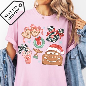 A woman wearing a pink t-shirt with various Christmas-themed illustrations, including a Santa hat, gingerbread houses, and other festive decorations.
