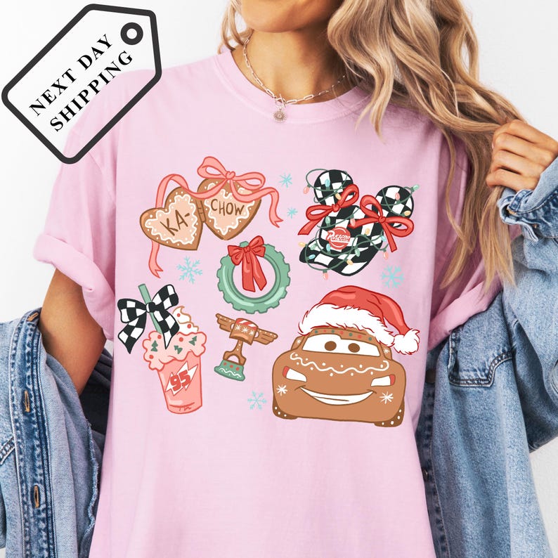 A woman wearing a pink t-shirt with various Christmas-themed illustrations, including a Santa hat, gingerbread houses, and other festive decorations.