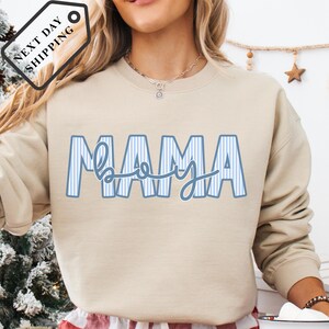 A woman wearing a beige sweatshirt with the word "MAMA" printed on it.