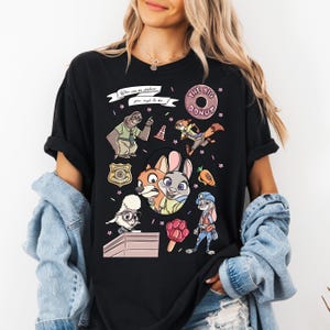 A woman wearing a black t-shirt with a colorful graphic design featuring various cartoon animal characters, including a dog, cat, and rabbit.