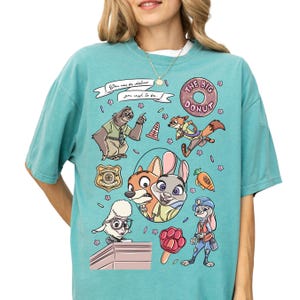 A woman wearing a teal-colored t-shirt with a colorful graphic design featuring various cartoon animal characters and a donut.
