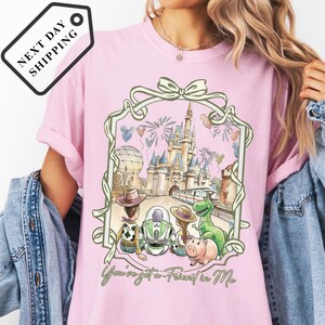 A pink t-shirt with a Disney-themed graphic design, including a castle, fireworks, and various Disney characters.