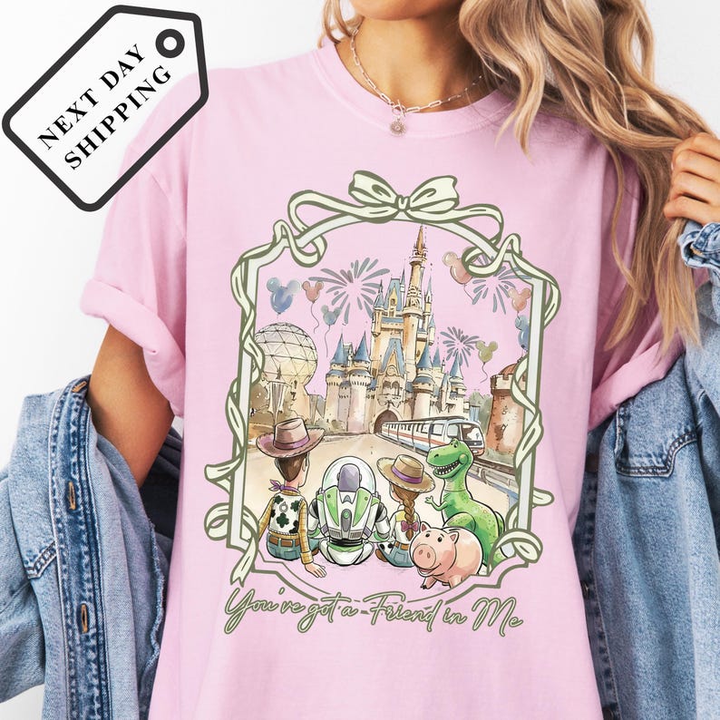 A pink t-shirt with a Disney-themed graphic design, including a castle, fireworks, and various Disney characters.