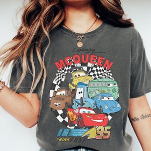 A person wearing a grey t-shirt with a graphic of various cartoon cars from the Cars movie franchise, including Lightning McQueen.