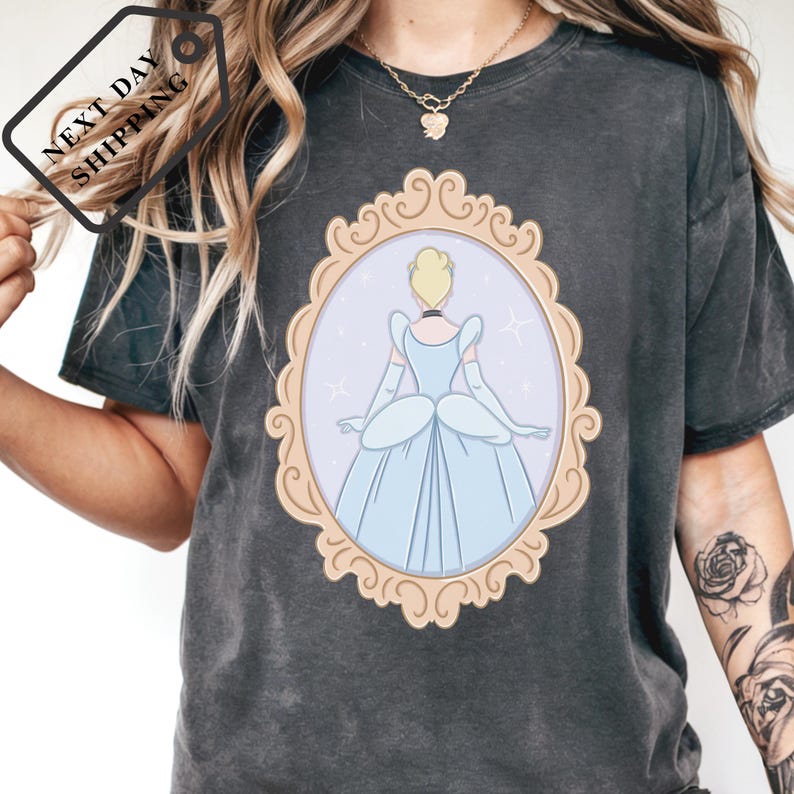 A person wearing a black t-shirt with a graphic of a woman in a blue dress, framed by an ornate golden border.