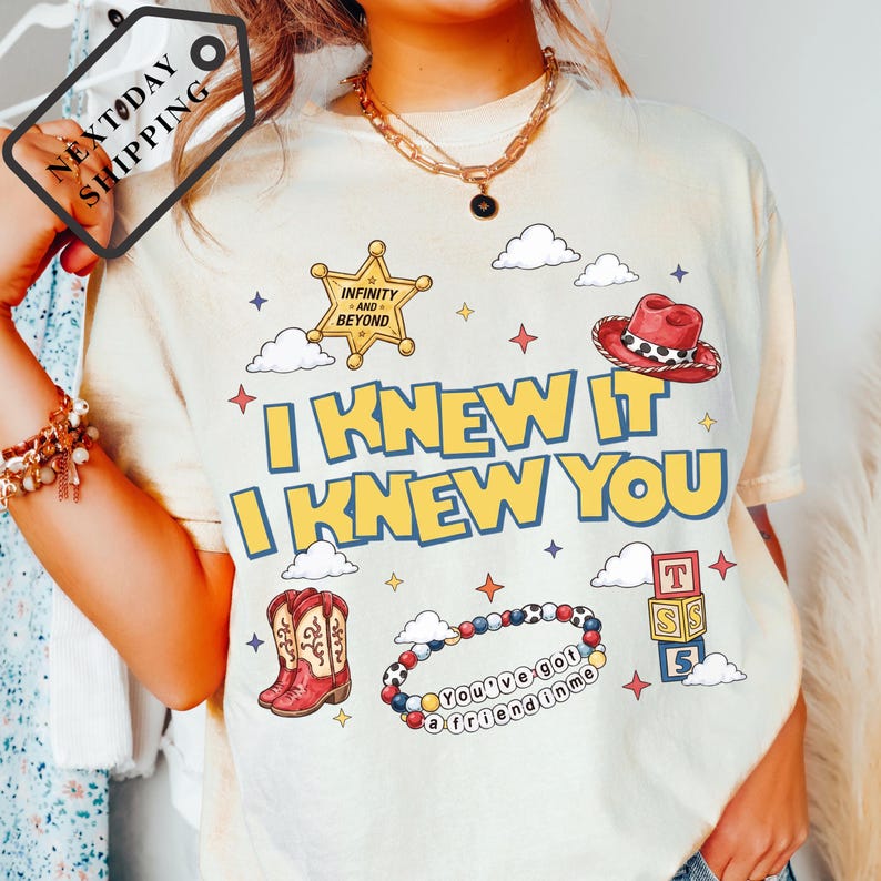 A person wearing a white t-shirt with a graphic design featuring a cowboy hat, clouds, and stars, along with the text "I KNEW IT I KNEW YOU" and other cartoon-style elements.