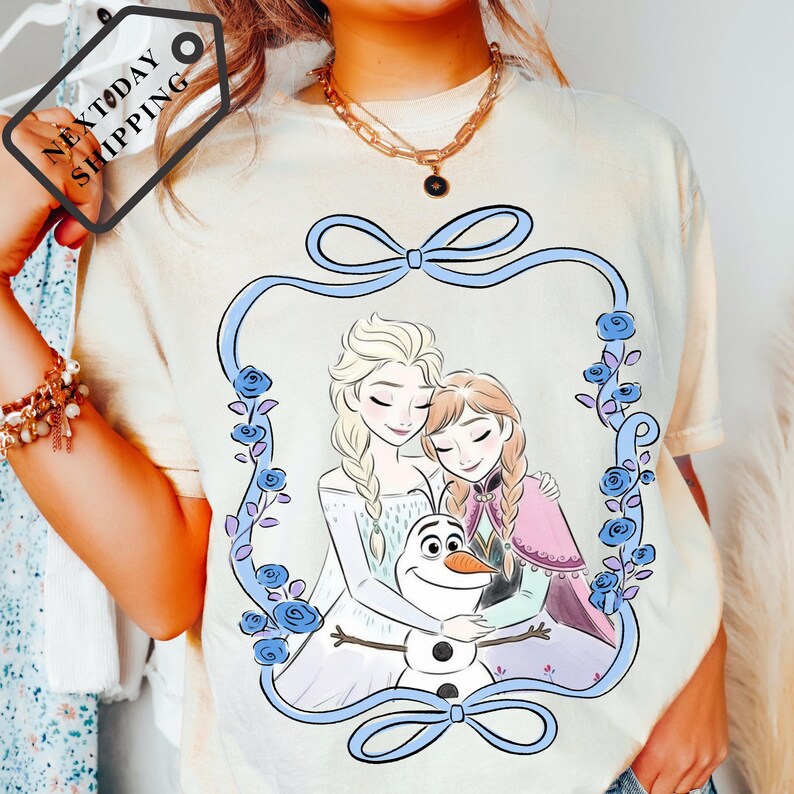 A person wearing a white t-shirt with a graphic design featuring two women and a snowman.