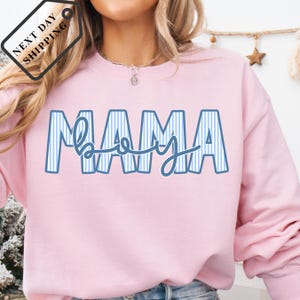 A woman wearing a pink sweatshirt with the word "MAMA" printed on it.