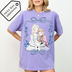 A woman wearing a purple t-shirt with a graphic design featuring characters from the Disney movie Frozen.