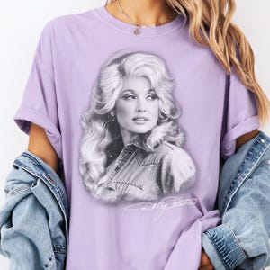 A person wearing a purple t-shirt with a portrait of a woman printed on it, along with a denim jacket.
