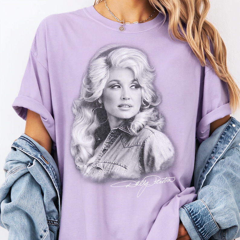 A person wearing a purple t-shirt with a portrait of a woman printed on it, along with a denim jacket.