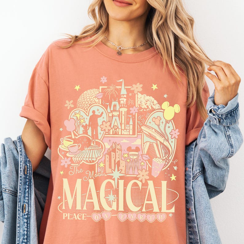 A woman wearing a pink t-shirt with a graphic design featuring various Disney-themed elements, such as Mickey Mouse, a castle, and flowers.