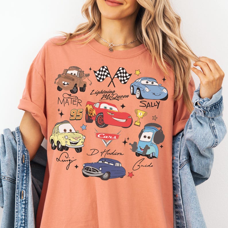 A woman wearing a pink t-shirt with various cartoon car characters and designs printed on it.