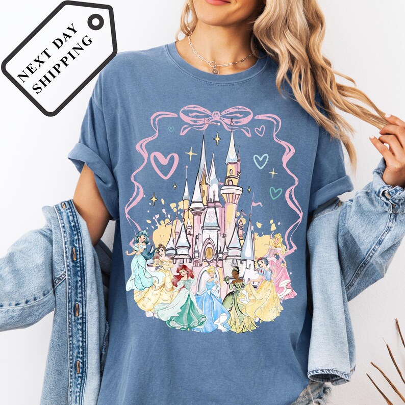 A woman wearing a blue t-shirt with a Disney princess castle design and various Disney characters.