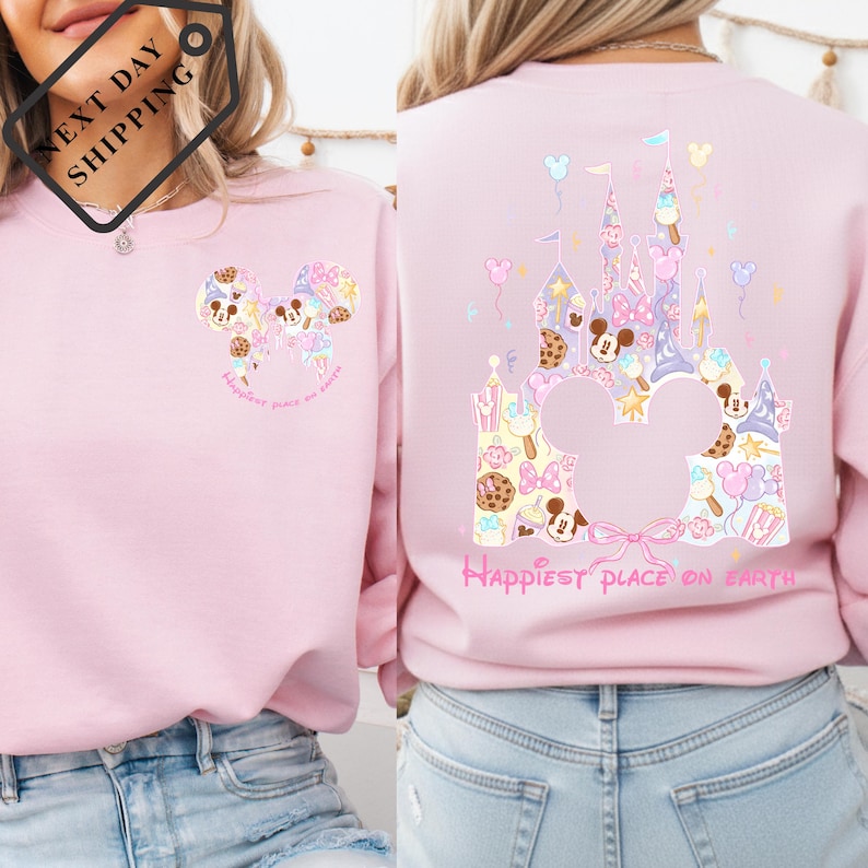 A woman wearing a pink sweatshirt with a Disney-themed design, including Mickey Mouse and a castle. The sweatshirt has a pink and white color scheme and features a message that says "Happiest place on earth".