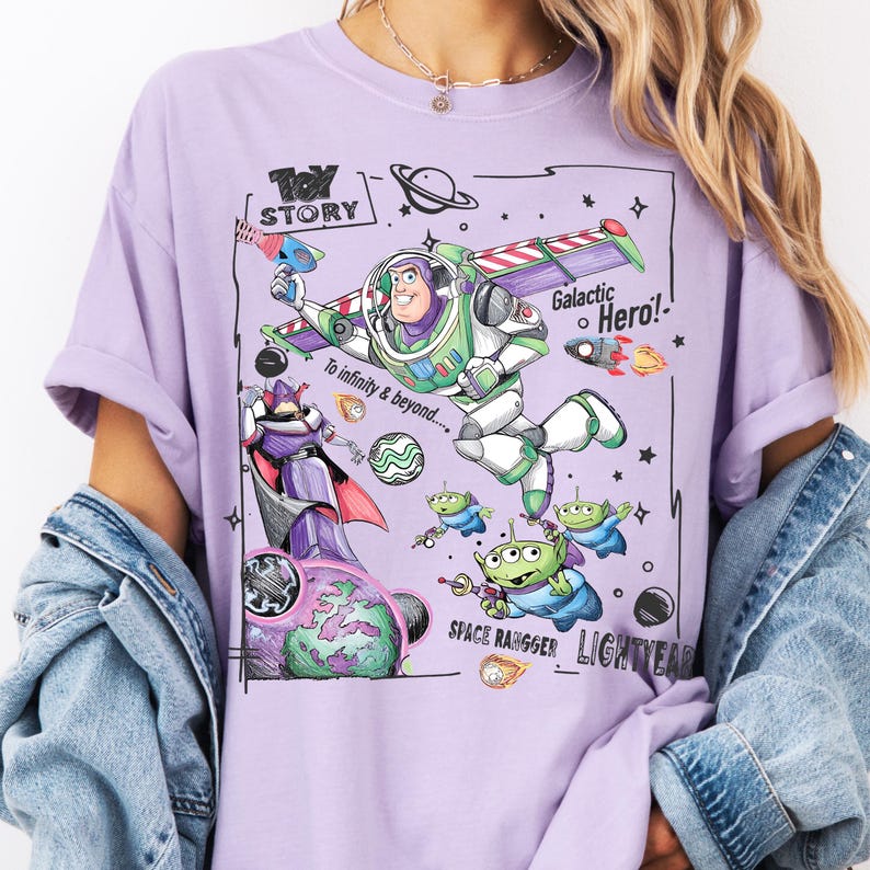A person wearing a purple t-shirt with a graphic design featuring characters from the Toy Story franchise, including Buzz Lightyear and a group of smaller alien characters.