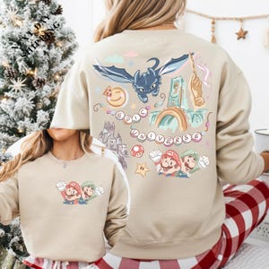 a woman wearing a beige sweatshirt with a colorful and whimsical design featuring Mario and other characters from the Super Mario video game franchise.