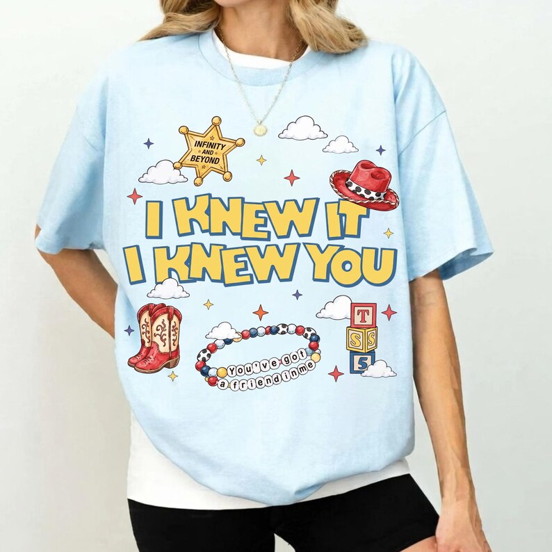 A woman wearing a light blue t-shirt with a graphic design featuring various cartoon-style icons and text.